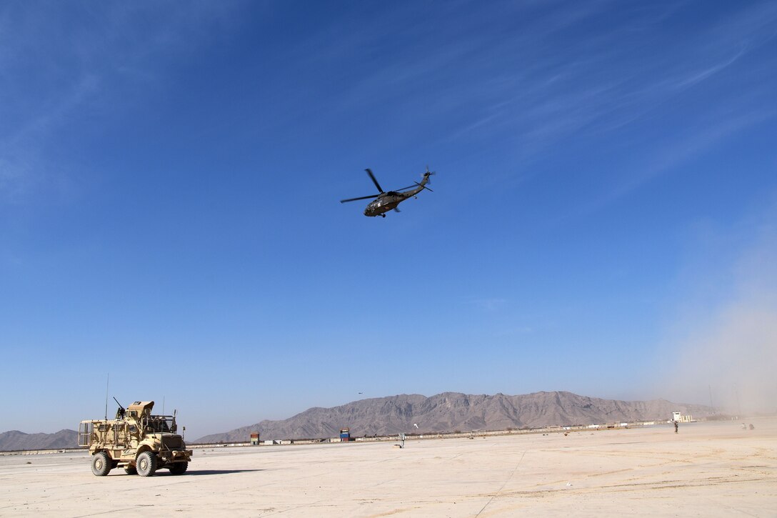 A helicopter flies in the sky above a military vehicle.