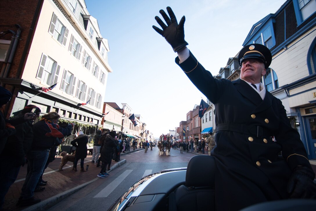 Army Command Sgt. Maj. John W. Troxell waves to a crowd from the backseat of a car.