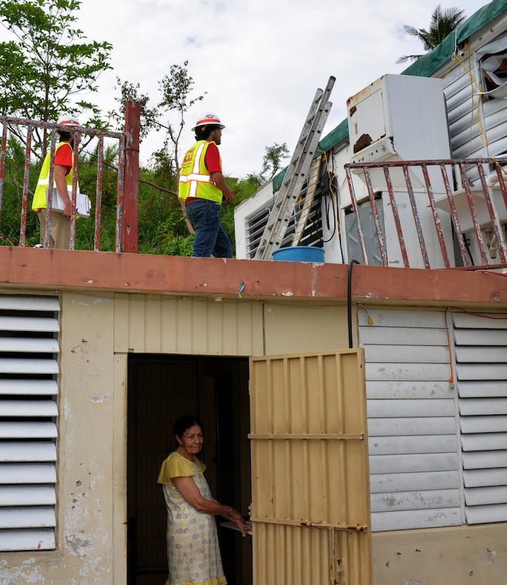 workers inspect roof while homeowner looks on