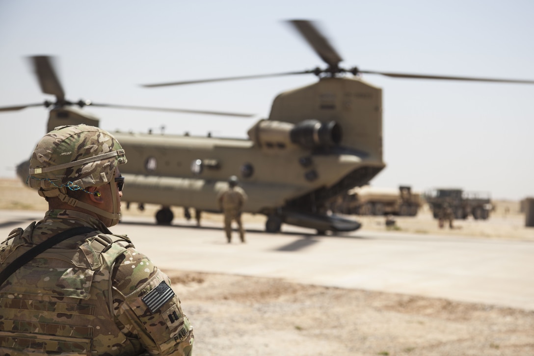 A soldier stands in front of a  CH-47 Chinook being refueled.