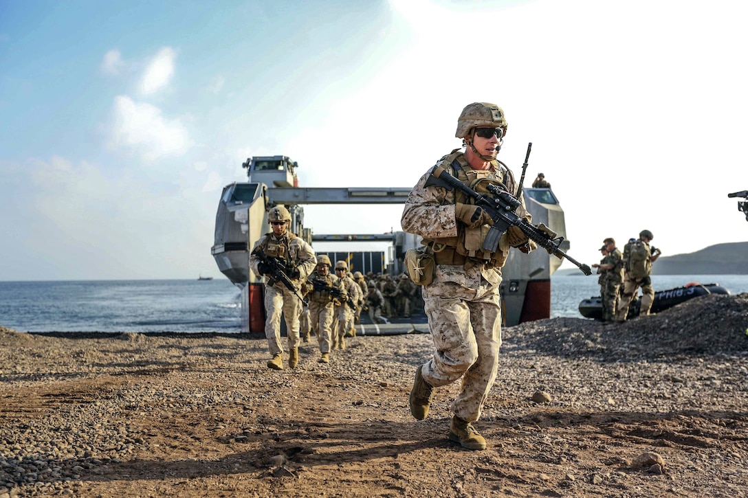 Marines run on the beach away from a landing craft.