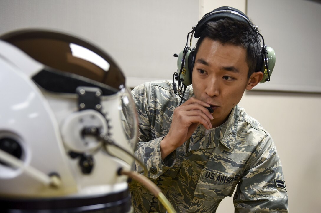 An airman with communicates with another airman in a pressurized suit.