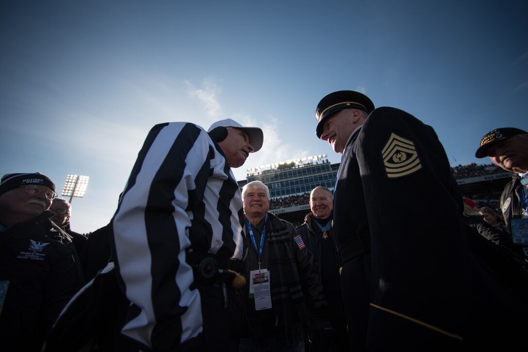 Army Command Sgt. Maj. John W. Troxell stands across from a football game referee.