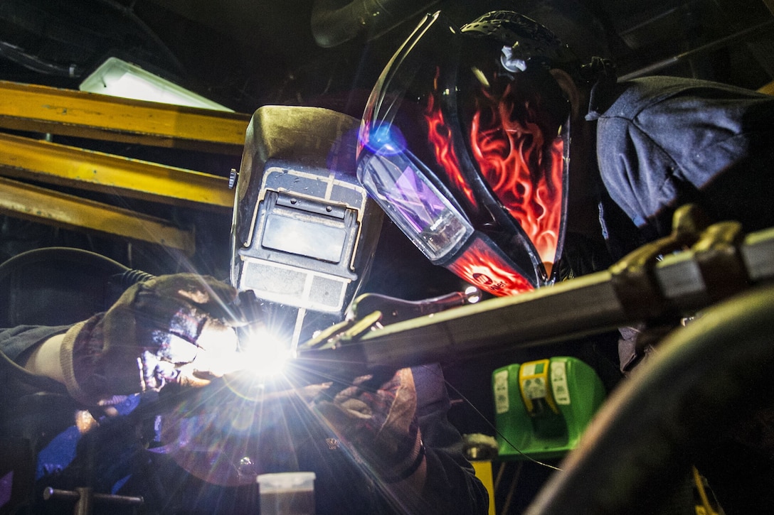 Two welders work on a railing with sparks flying.