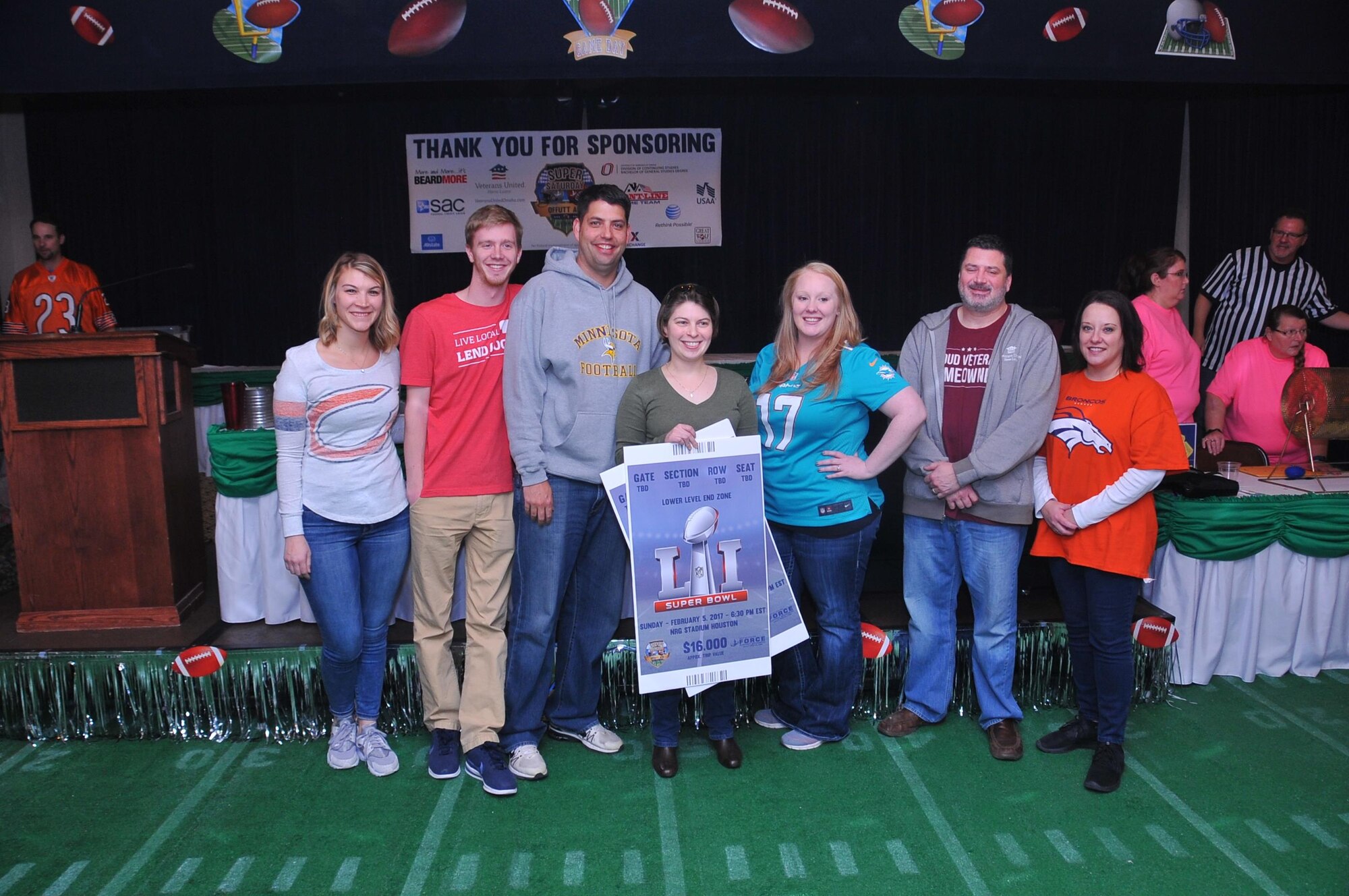 Nick Schuster, in the gray Minnesota Football sweatshirt of Veterans United Home Loans, the title sponsor for Super Saturday is seen here with his staff and the Super Saturday Bingo winner Maj. Kelly Borukhovich,20th Intelligence Squadron, to his right. The Offutt Air Force Base’s Super Saturday event was at the Patriot Club on Jan. 21. The event included live and silent auctions of sports mermorbelia and Bingo to determine who wins the grand prize of an all expenses paid trip for two to Super Bowl LI. (U.S. Air Force photo by D.P. Heard)