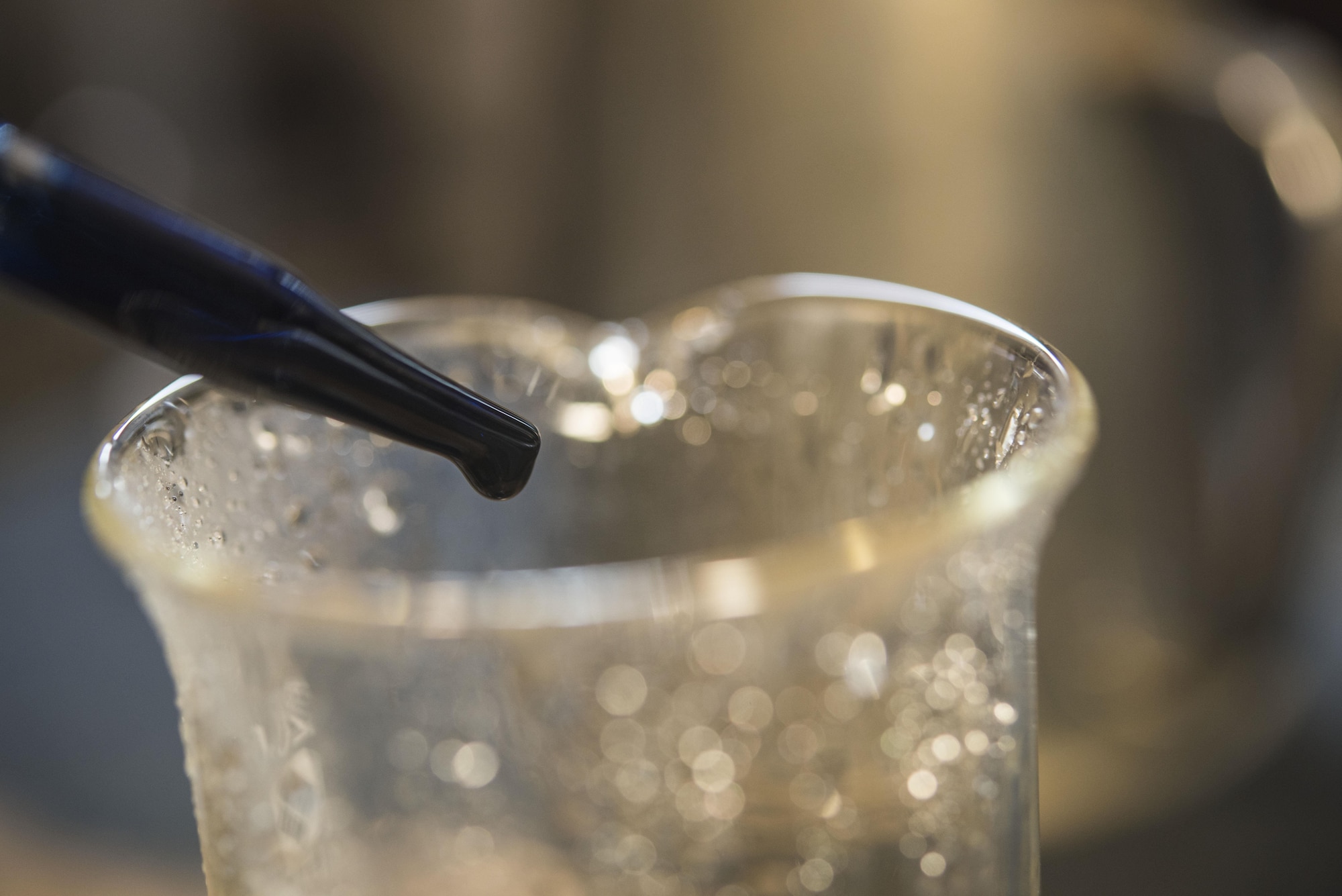 A drop of Black-T chemical drips into a glass measuring cup filled with water at Misawa Air Base, Japan, Jan. 30, 2017. Black-T is a multi-step process which employs a series of chemically bonding products through the pipes, providing protection against rust, corrosion and external damage. During a maintenance check, boiler technicians mix in one drop of the chemical mixture to the water circulating through the boilers. (U.S. Air Force photo by Airman 1st Class Sadie Colbert)