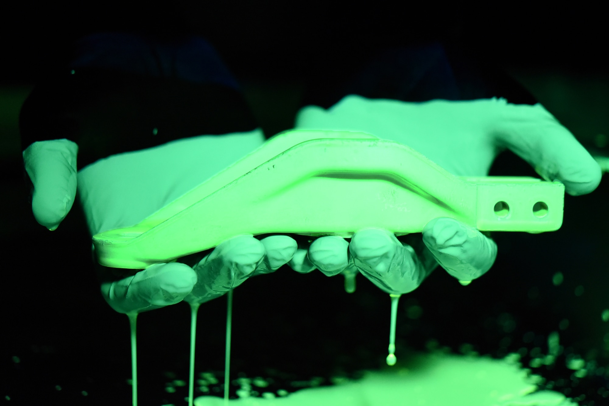 U.S. Air Force Airman 1st Class James Schwein, 19th Maintenance Squadron nondestructive inspections journeyman, holds an aircraft tow fitting arm after dipping it into fluorescent penetrant at Little Rock Air Force Base, Ark. The penetrant seeps into tiny openings in the part to identify potential cracks. (U.S. Air Force photo by Airman 1st Class Kevin Sommer Giron)