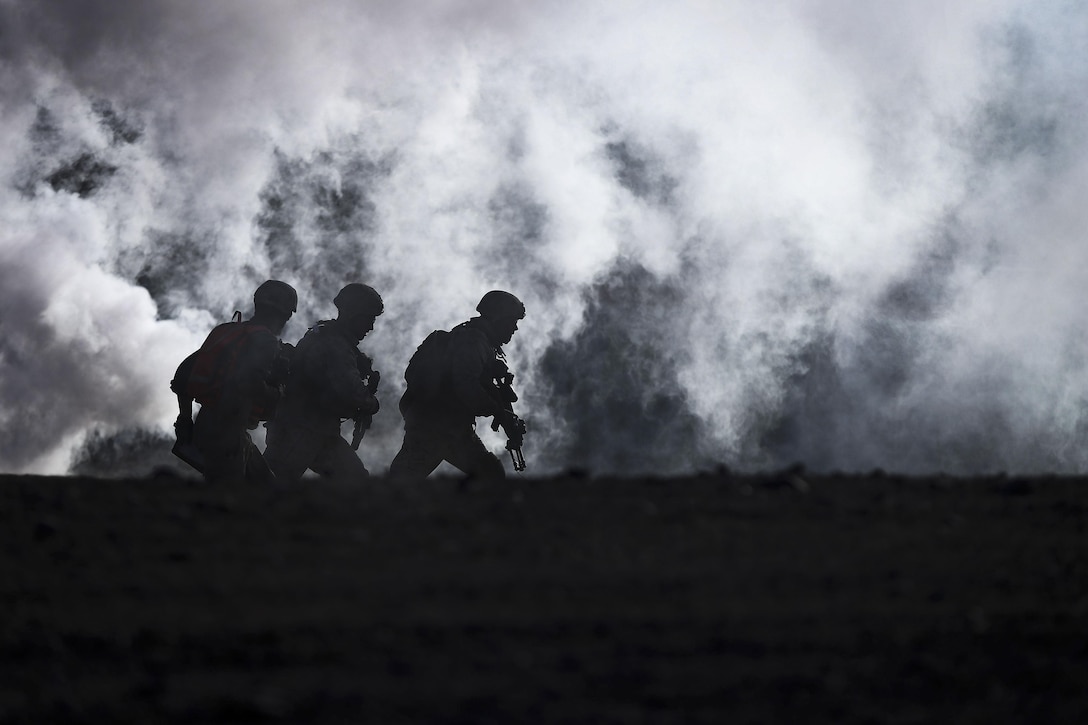 Three Marines, shown in silhouette, run as smoke billows behind them.