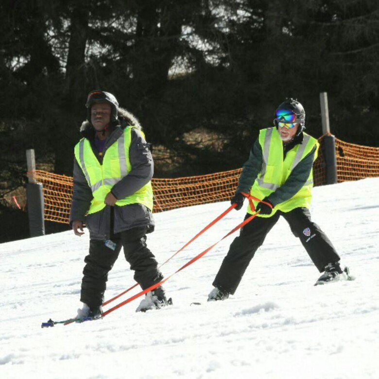 Marcus Brumbaugh, an electrical mechanic from the Nashville District uses a radio telephone headset inserted inside helmets to communicate and guide Mamadi Corra, a PhD professor at East Carolina University and adaptive skier down a slope during the 36th Disabled Sports USA Adaptive Learn to Ski event clinic held Jan. 19, 2017 at the Beech Mountain Resort in Beech Mountain, N.C.   The instructor.  