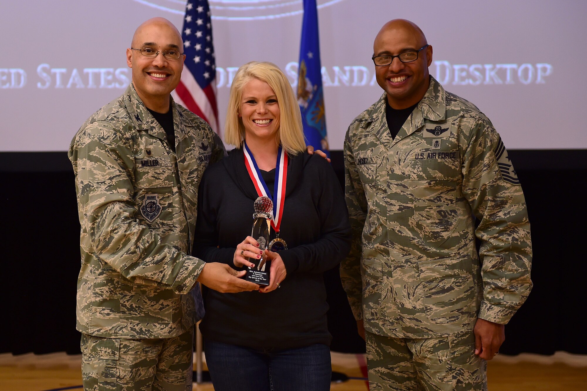 Autumn Hammer, Buckley key spouse, center, receives the Key Spouse of the Year Award, from Col. David Miller Jr., 460th Space Wing commander, and Chief Master Sgt. Rod Lindsey, 460th SW command chief, Feb. 3, 2017, at the annual awards on Buckley Air Force Base, Colo. The annual awards is a ceremony that recognizes the significant achievements, dedication and skill of the military and civilian members of the 460th SW. (U.S. Air Force photo by Airman Jacob Deatherage/Released)