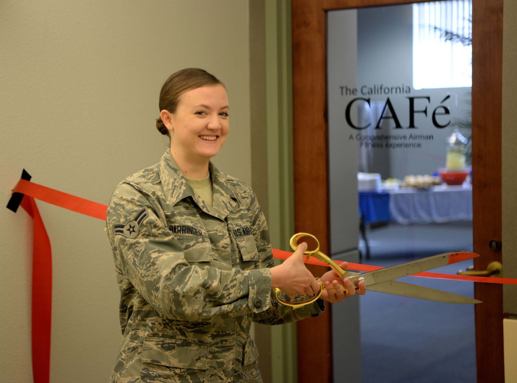 Airman First Class Aubrey, 9th Intelligence Squadron quality assurance specialist cuts the ribbon at the opening of the California CAFé, at the Beale Community Activity Center, Feb. 3, 2017, at Beale Air Force Base, California. CAFé is acronym for Comprehensive Airmen Fitness Experience. The CAFé lounge offers free coffee, Wi-Fi, and a full surround sound projection screen. (U.S. Air Force photo/ Staff Sgt. Bobby Cummings)