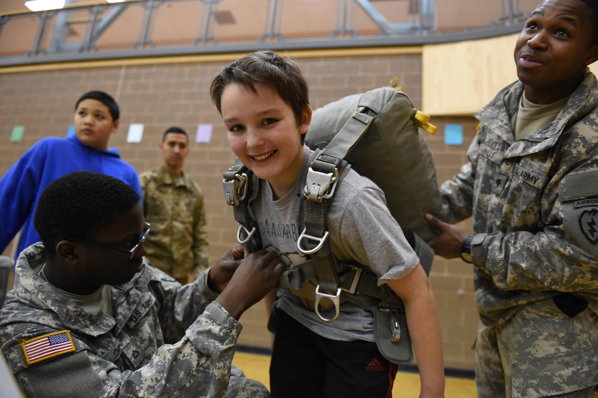 Pfc. Philip Chery, and Spc. Robert Walls, parachute packers with the 4th Quartermaster Company, 725th Brigade Support Battalion (Airborne), 4th Brigade Combat Team (Airborne), 25th Infantry Division, U.S. Army Alaska, help R.J. Nelson, 11, don the T-11 parachute at Begish Middle School, Feb. 2, 2017. Headquarters and Headquarters Company, 4th Brigade Combat Team (Airborne), 25th Infantry Division Soldiers were one of many Science, Technology, Engineering, Art and Math presenters who interacted with about 300 students at the school's Career Fair. The fair is one of several annual events the unit's Soldiers support at the school as part of the Joint Base Elmendorf-Richardson School Partnership Program. 