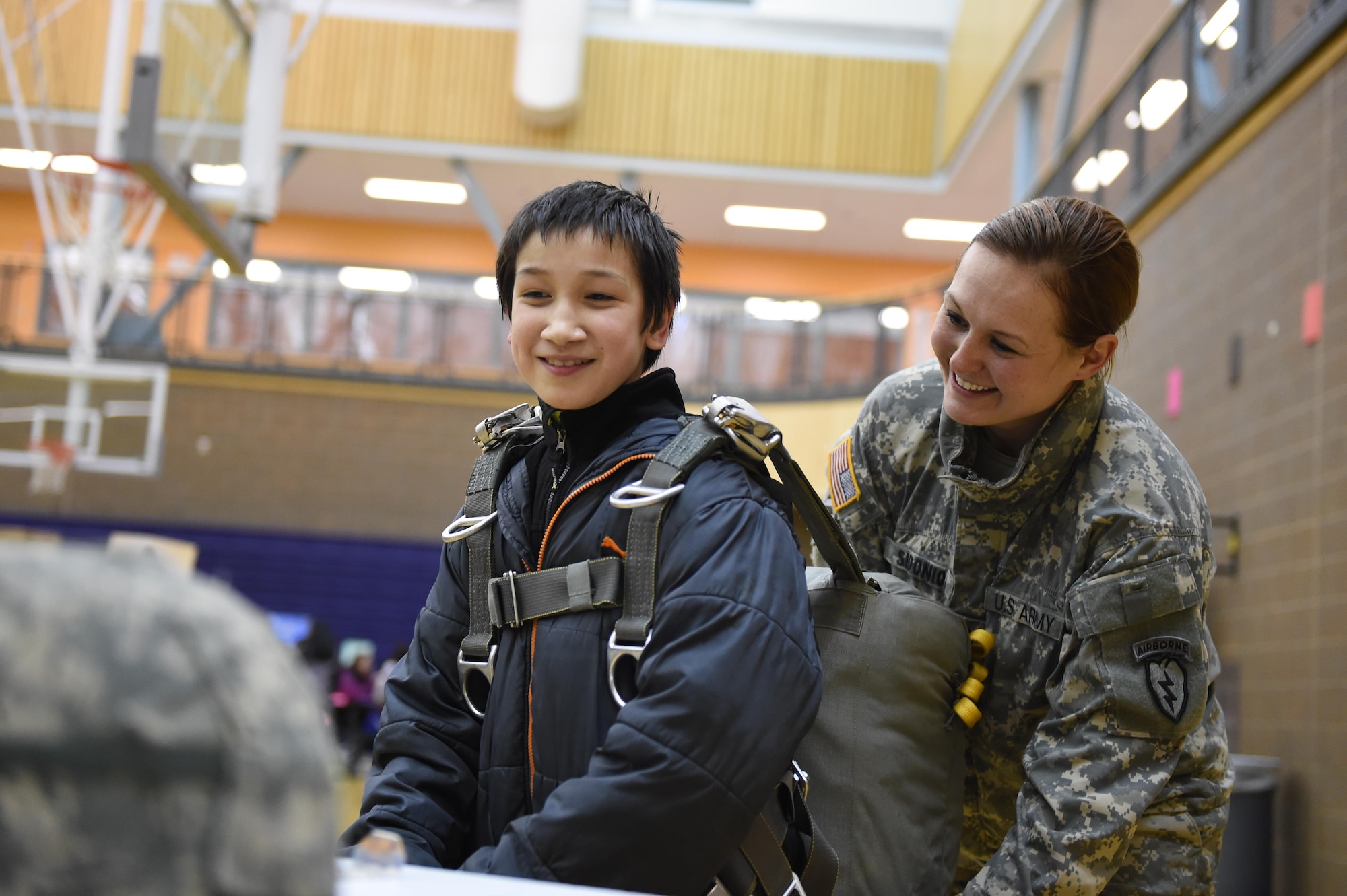Sgt. 1st Class Amanda Sidonio of the Headquarters and Headquarters Company, 4th Brigade Combat Team (Airborne), 25th Infantry Division, helps Robert Wendt, 11, strap a T-11 parachute on Begich Middle School Principal Brian Singleton at Begich Middle School. Feb. 2, 2017. The HHC, 4-25th IBCT Soldiers were one of many Science, Technology, Engineering, Art and Math presenters who interacted with about 300 students at the school's Career Fair. The fair is one of several annual events the unit's Soldiers support at the school as part of the Joint Base Elmendorf-Richardson School Partnership Program. 