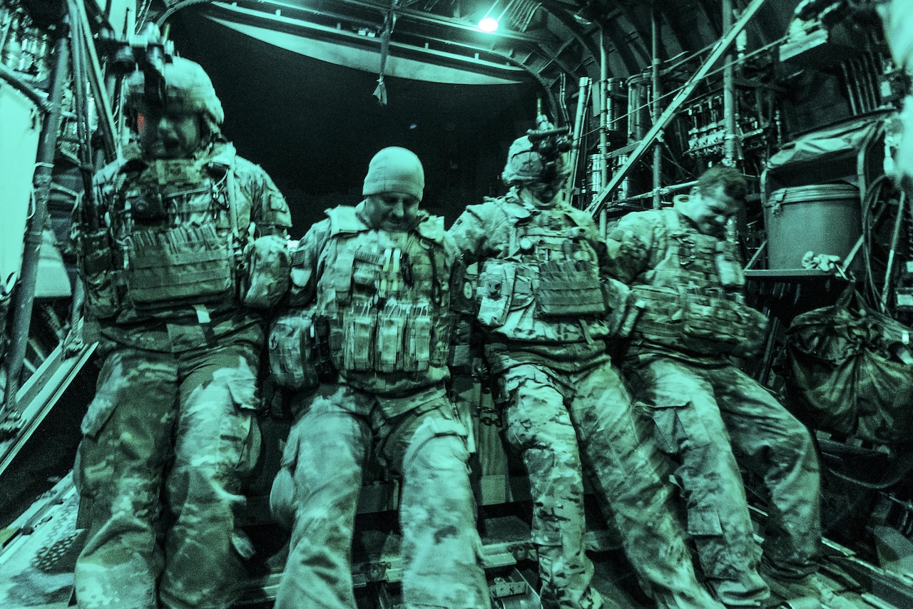 Four airmen, illuminated by green light, lean into a load of cargo to push it onto an aircraft.