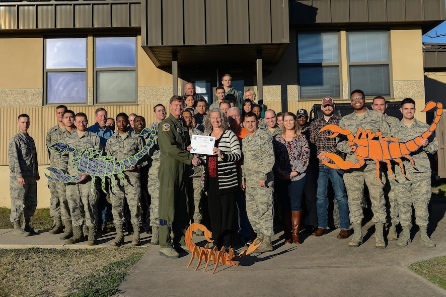 Linda Herzog, 47th Communications Squadron wing information systems security manager (front center), accepts the “XLer of the Week” award from Col. Thomas Shank, 47th Flying Training Wing commander (front left), and Chief Master Sgt. George Richey, 47th FTW command chief (front right), on Laughlin Air Force Base, Texas, Jan. 25, 2017. The XLer is a weekly award chosen by wing leadership and is presented to those who consistently make outstanding contributions to their unit and Laughlin. (U.S. Air Force photo/Airman 1st Class Benjamin N. Valmoja)