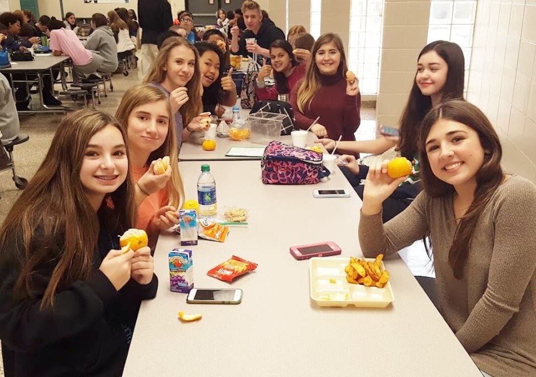 Students at Discovery Middle School in Madison, Alabama hold up their Alabama-grown satsumas during lunch. DLA Troop Support’s Subsistence supply chain provides satsumas to Alabama schools through Department of Defense Fresh program. 