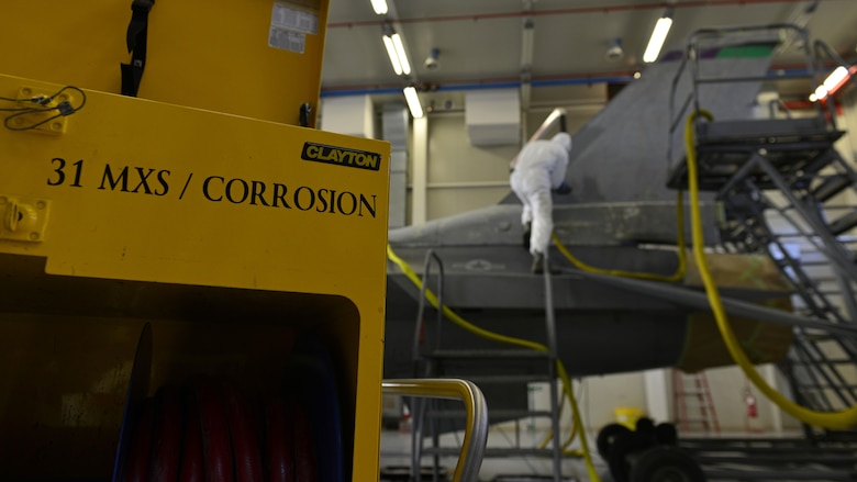 An Airman from the 31st Maintenance Squadron Corrosions flight sands paint off an F-16 Fighting Falcon tail at Aviano Air Base, Italy, Jan. 23, 2017. The corrosions flight Airmen sanded the paint off before painting on a new design. (U.S. Air Force photo by Senior Airman Cary Smith)