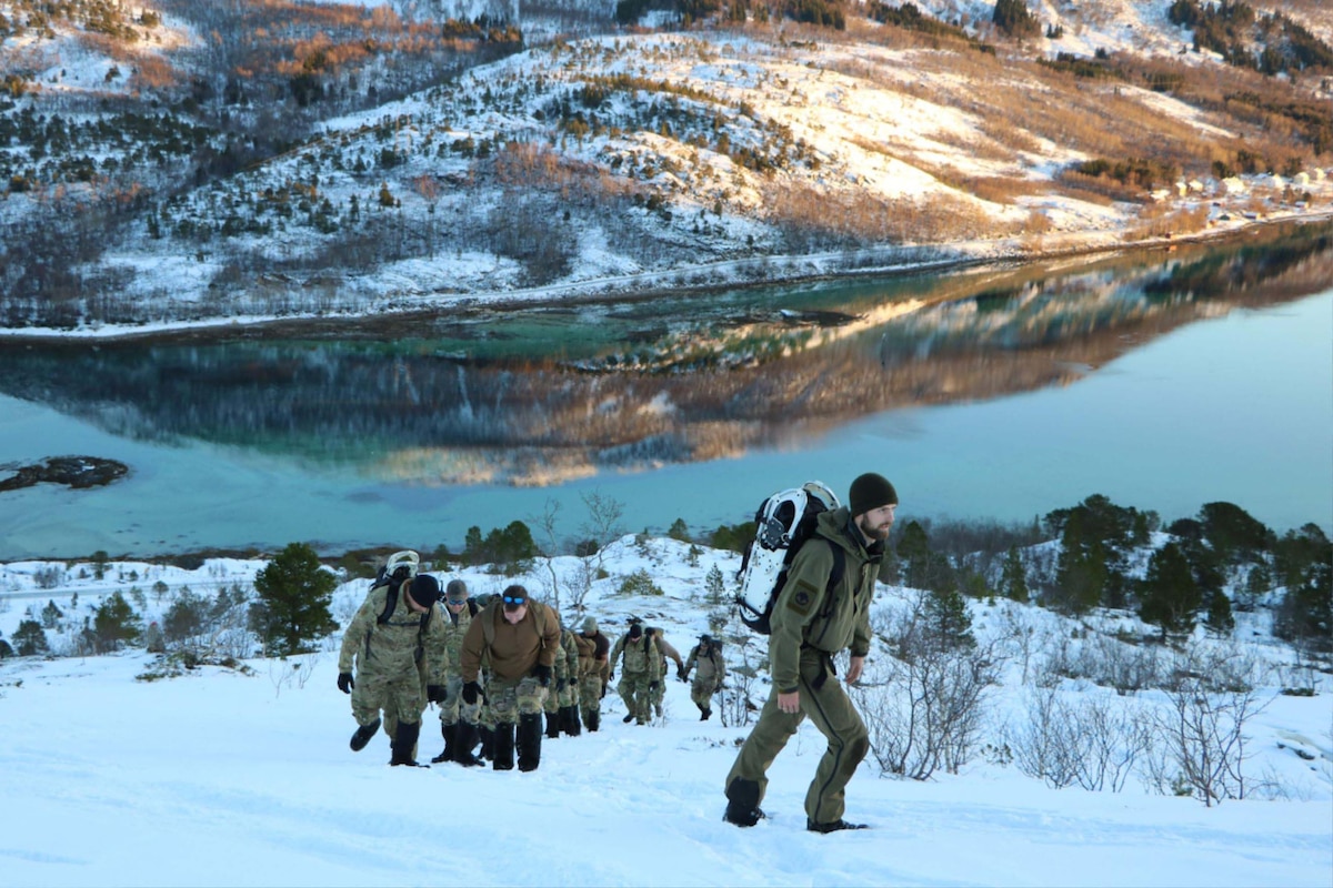 U.S. and Norwegian troops trek through snow uphill.