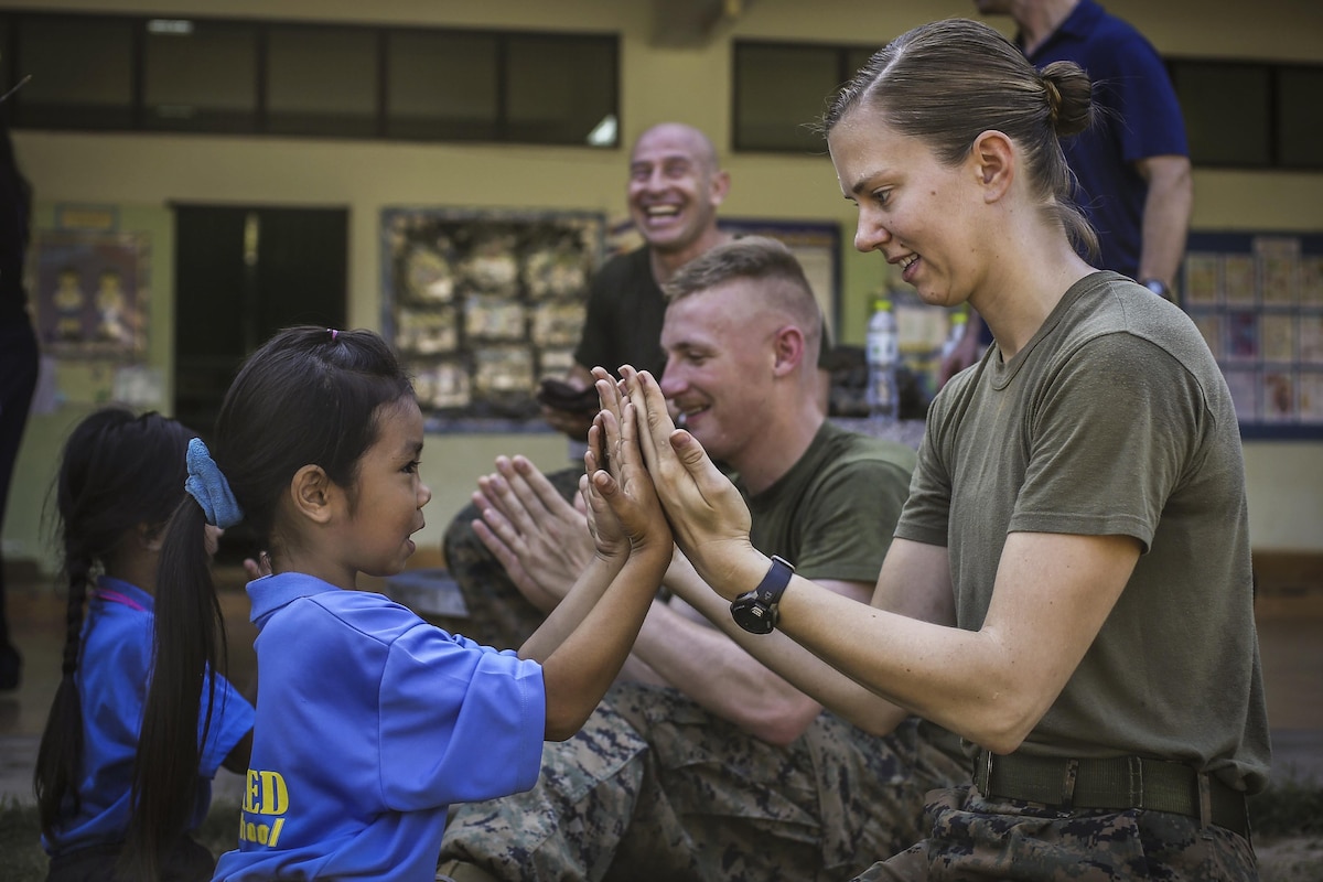A Marine plays hand games with a girl student at a school.