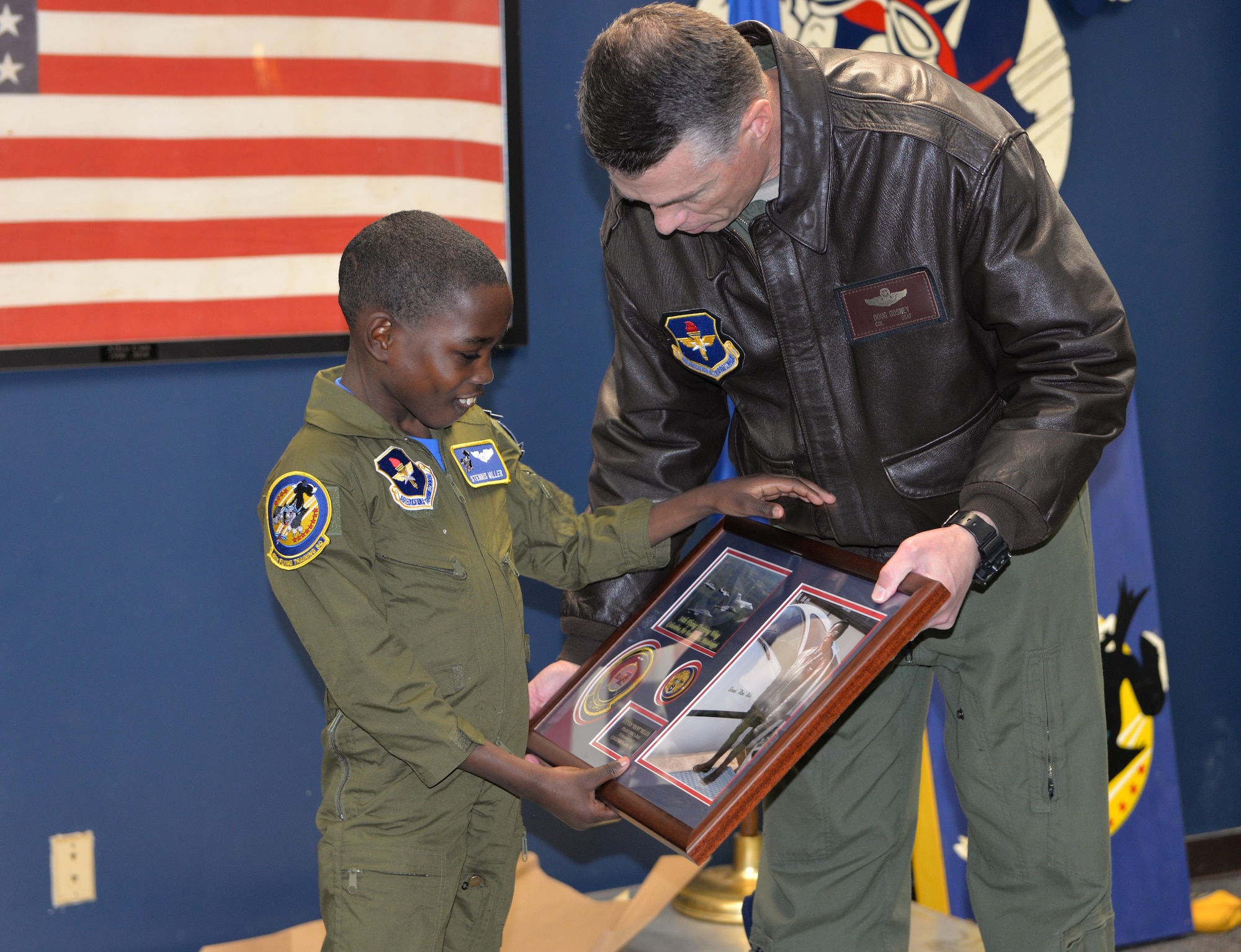 Col. Douglas Gosney, 14th Flying Training Wing Commander, hands Stennis Miller, 14th FTW “Pilot for a Day,” a plaque of his hero shot and coin commemorating his time on base Feb. 3, 2017, at Columbus Air Force Base, Mississippi. In partnership with the Columbus-Lowndes Chamber of Commerce, children with life-long illnesses get a chance to experience a day with the Air Force custom-tailored to their desires and capabilities. (U.S. Air Force photo by 2nd Lt. Savannah Stephens)