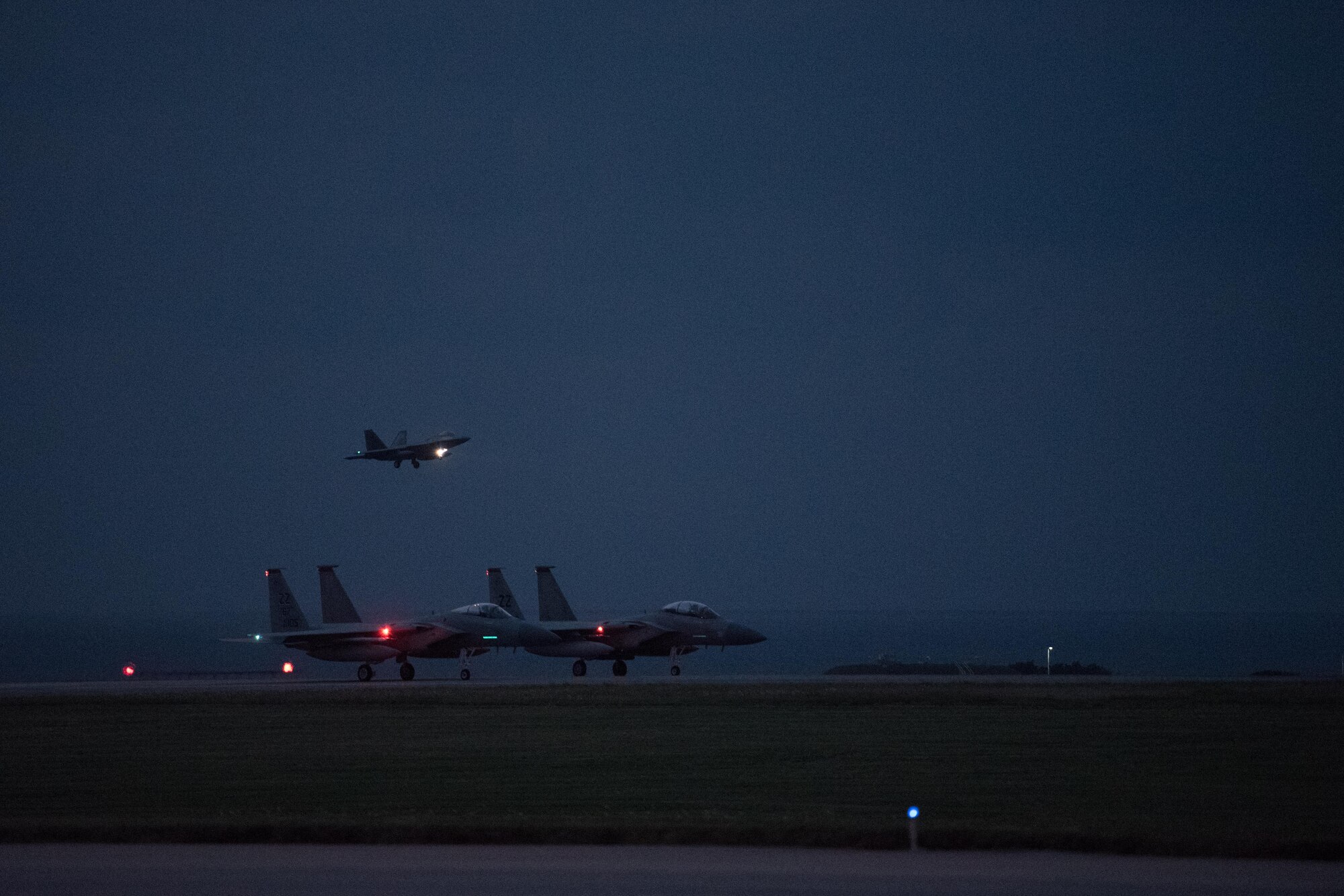 A U.S. Air Force F-22 Raptor from the 90th Fighter Squadron lands at Kadena Air Base, Japan, while F-15 Eagles from the 67th Fighter Squadron taxi on the flightline Feb. 7, 2017. The F-22 Raptors stopped at Kadena AB before traveling on to Royal Australian Air Force Base, Tindal. As allies, the U.S. and Australia have agreed to more frequent movements of aircraft across the Indo-Asia-Pacific region.  (U.S. Air Force photo by Senior Airman Omari Bernard/Released)