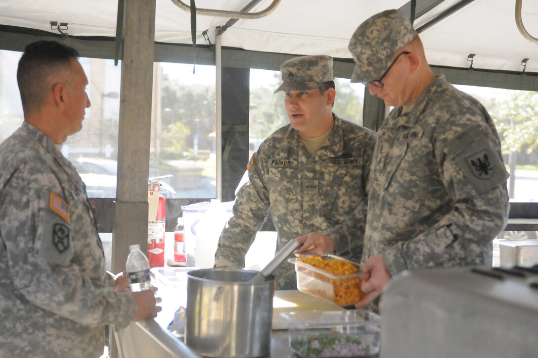 Army Reserve Warrant Officer Candidate Joseph Parker, 143rd Sustainment Command (Expeditionary), and CW2 Colby Beard, 11th Theater Aviation Command, both with the Army Reserve Culinary Arts Team, discuss the meal plan with the 143rd ESC Food Services Officer while preparing a meal out of a mobile kitchen trailer at the Orlando Armed Forces Reserve Center. Parker, Beard, and the Army Reserve Culinary Arts Team were rehearsing for the upcoming 42nd Annual Military Culinary Arts Competition.