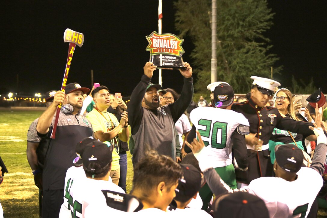 The coach for Victor Valley High School raises the Great American Rivalry Series Trophy Oct. 7. Victor Valley beat Barstow High School to claim the title. 