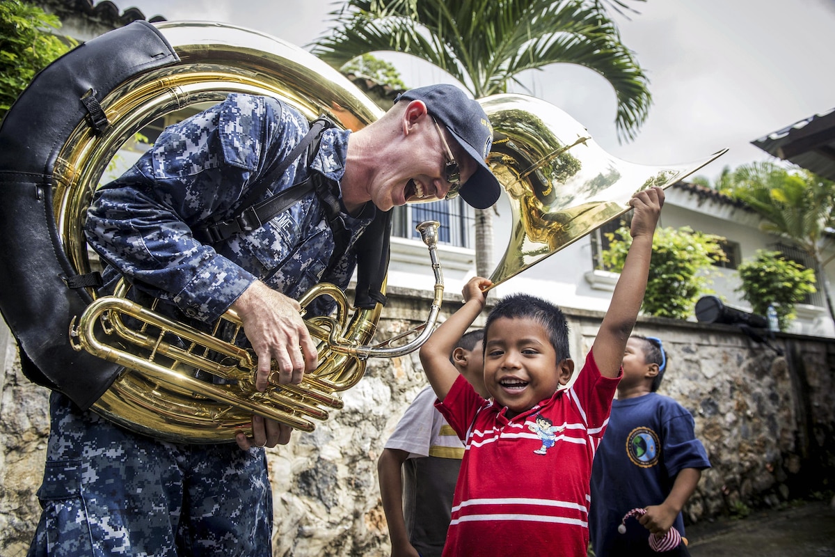 A sailor plays a musical instrument with a child.