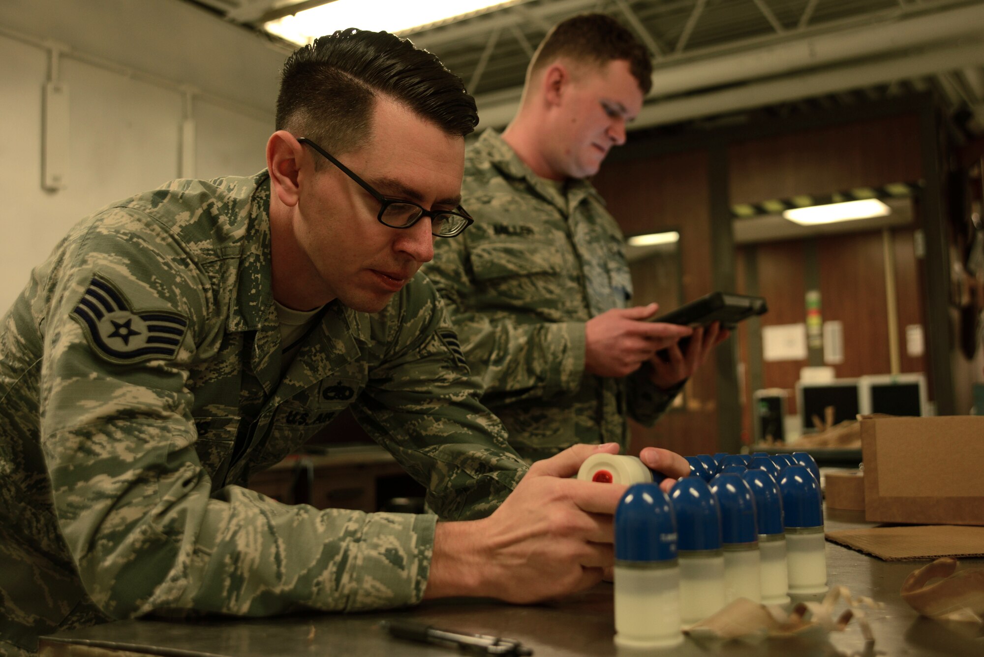 U.S. Air Force Staff Sgt. Ralph Simons, 20th Equipment Maintenance Squadron munitions inspector, left, visually inspects 40 mm grenades while Staff Sgt. Cameron Miller, right, 20th EMS munitions inspector, reads technical orders at Shaw Air Force Base, S.C., Feb. 6, 2017. Technical orders list detailed tasks that must be completed by munitions inspectors to ensure munitions will function properly. (U.S. Air Force photo by Airman 1st Class Kathryn R.C. Reaves)
