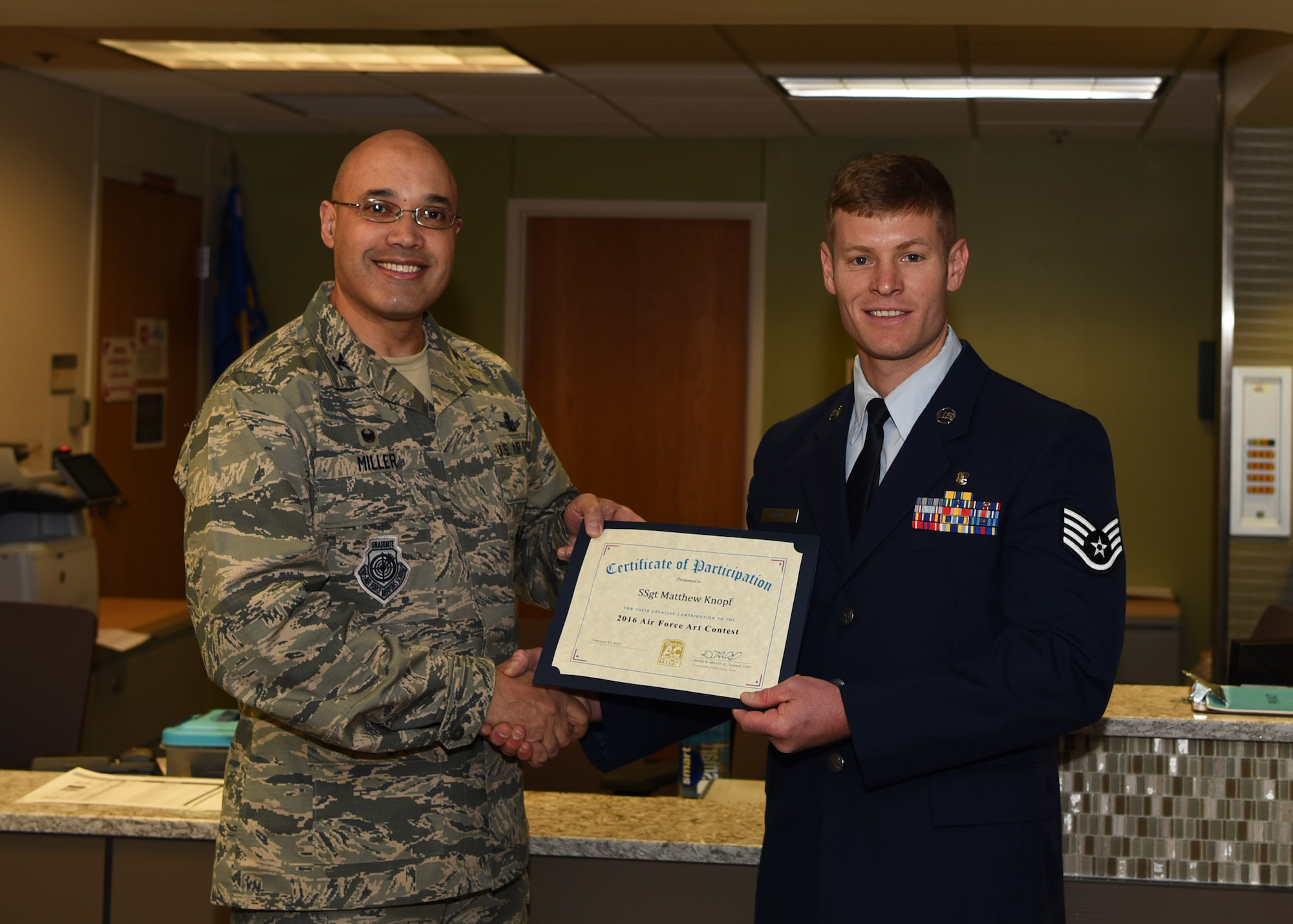 Col. David Miller Jr., 460th Space Wing commander, presents Staff Sgt. Matthew Knopf, 310th Aerospace Medical Flight health services management supervisor, with a certificate for his accomplishment of winning the 2016 Air Force Art Contest in the accomplished artist category Feb. 12, 2017, on Buckley Air Force Base, Colo. Knopf’s painting was selected from a total of 326 entries in the adult accomplished artist category. (U.S. Air Force photo by Airman Holden S. Faul/ Released)