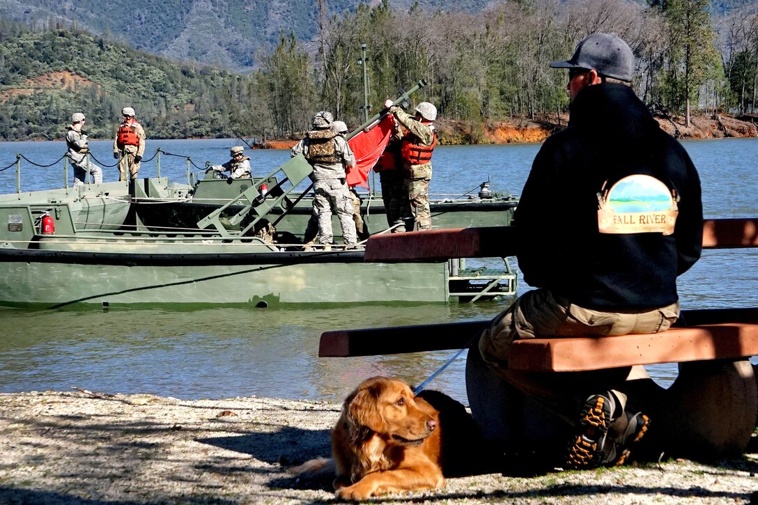 A local and his dog watch as Army National Guard soldiers finish assembling a temporary pontoon bridge during training at Whiskeytown Lake, near Redding, Calif., Feb. 11, 2017. The unit invited members of the local area to come out and watch the training and learn about the work they were doing. Army National Guard photo by Spc. Amy E. Carle 