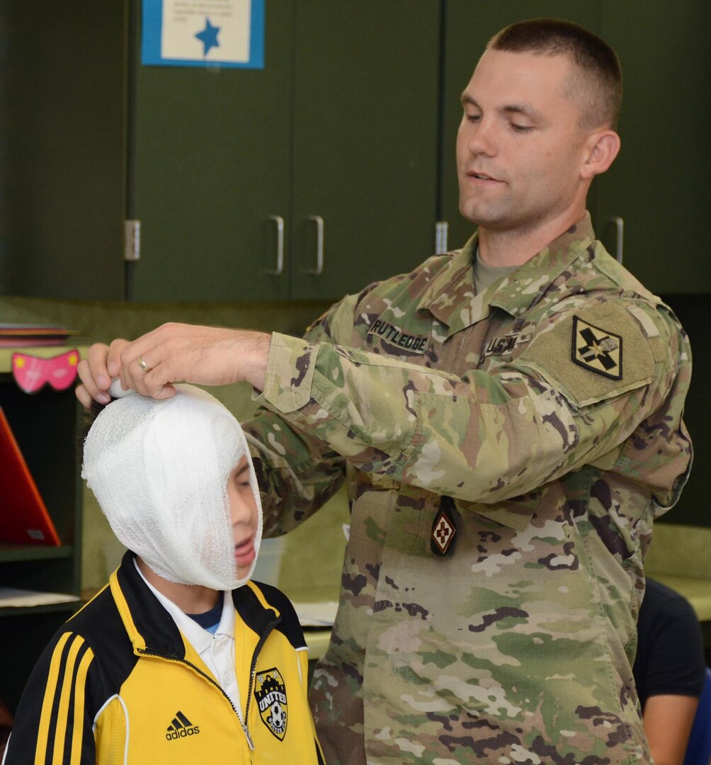 Sgt. 1st Class Roy Rutledge from the 264th Medical Battalion demonstrates placing a head bandage on an East Terrell Hills Elementary School student during the school’s career day.