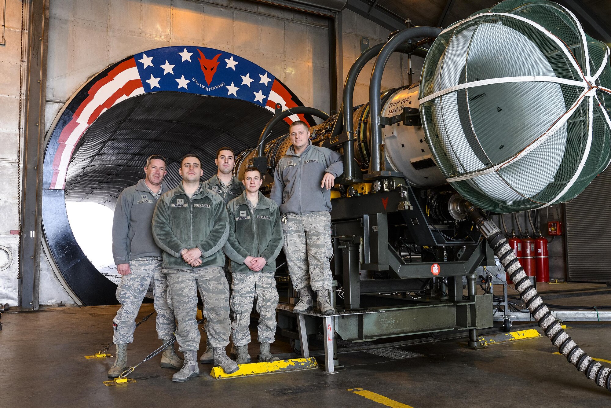 A picture of Air National Guardsmen from New Jersey's 177th Fighter Wing pose for a photo in front of the morale painting they designed, funded and created at the engine test cell facility.