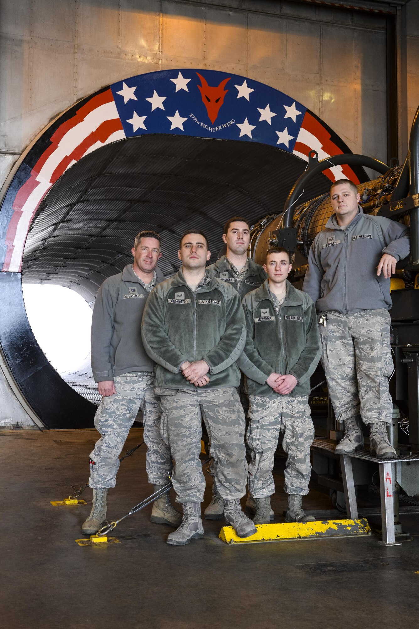 A picture of Air National Guardsmen from New Jersey's 177th Fighter Wing pose for a photo in front of the morale painting they designed, funded and created at the engine test cell facility.