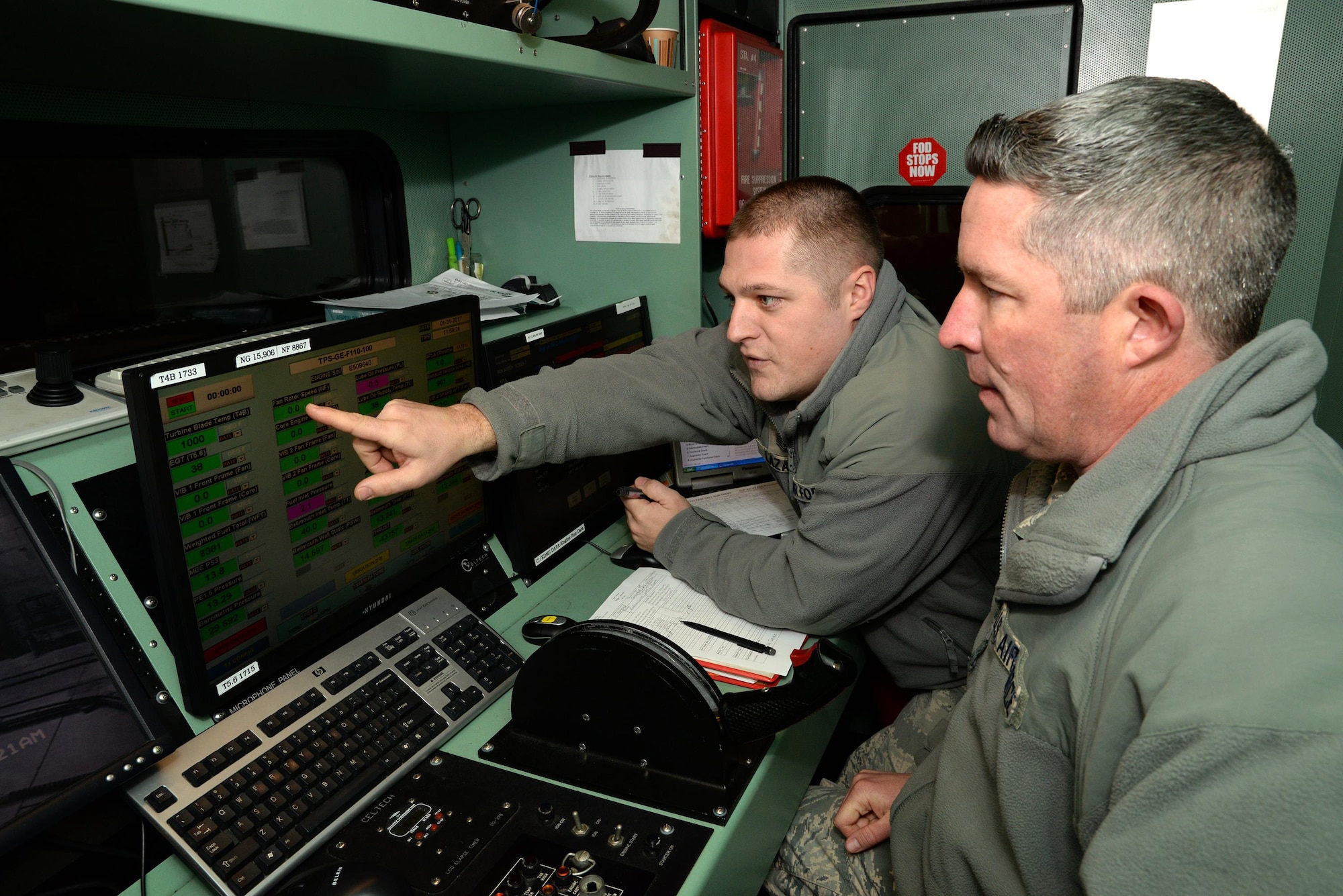 A picture of U.S. Air Force Master Sgt. Andre Lazaro, engine test cell supervisor with the 177th Fighter Wing of the New Jersey Air National Guard, pointing to a fan rotor speed indicator while Tech. Sgt. Robert Taylor, propulsion mechanic, prepares to fire up an engine from an F-16C+ Fighting Falcon.