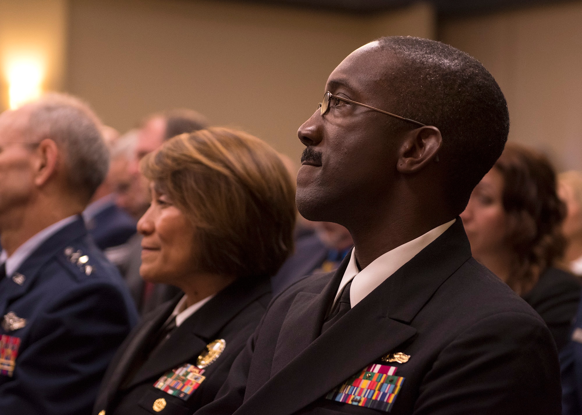 Navy Capt. James Ellzy, Defense Health Management Systems executive officer, watches a guest speaker during a "go-live" recognition ceremony for MHS Genesis Feb. 15, 2017, at Fairchild Air Force Base, Wash. Ellzy was the master of ceremonies during the event. (U.S. Air Force photo/Airman 1st Class Ryan Lackey)