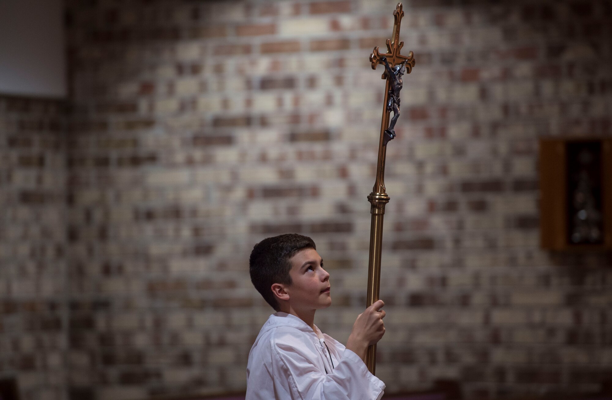 An altar boy carries a cross down the aisle to begin Confirmation Mass, Feb. 14, 2017, at Moody Air Force Base, Ga. Pope John Paul II created the Archdiocese for the Military Services in 1985 to provide the Catholic Church's full range of pastoral ministries and spiritual services to those in the United States Armed Forces. The Archbishop for the Military Services is responsible for the spiritual welfare of more than 1.8 million men, women and children. (U.S. Air Force photo by Andrea Jenkins/Released)