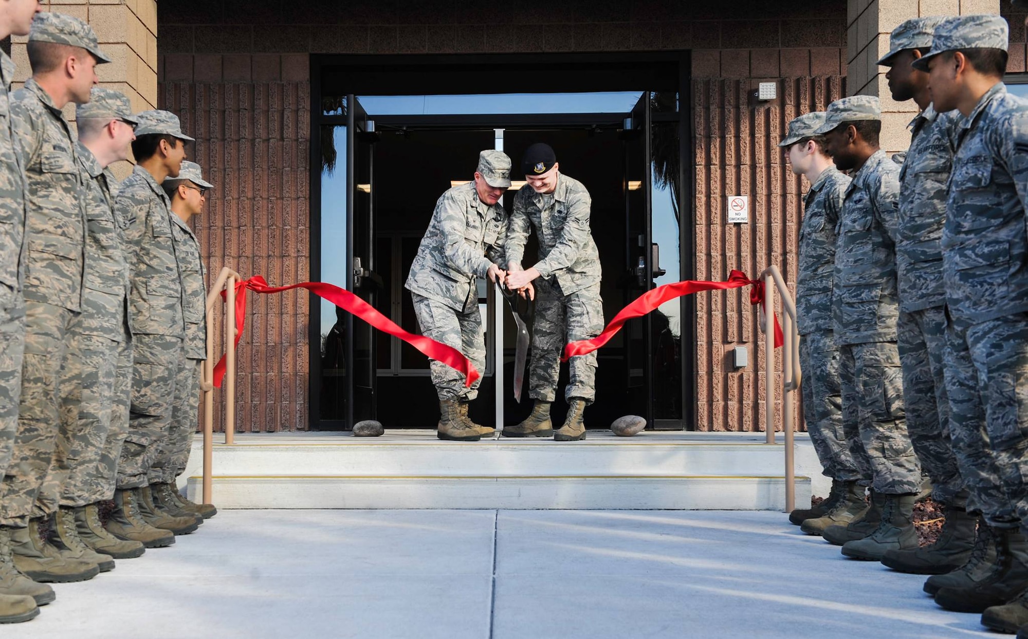 Col. Paul Murray, 99th Air Base Wing commander, and Airman 1st Class Nicholas Martini, 99th Security Forces Squadron, cut the ceremonial ribbon for the new dormitory during a ceremony on Nellis Air Force Base, Nev., Feb. 3, 2017. The new facility’s amenities include ample parking spaces, basketball court, sand volleyball court, and multiple shaded outdoor seating areas. (U.S. Air Force photo by Airman 1st Class Kevin Tanenbaum/Released)