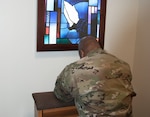 Army Capt. Demetrius Walton, DLA’s deputy command chaplain, kneels in prayer in the McNamara Headquarters Complex’s newly renovated prayer and meditation room. Above him is an LED light box that depicts a stained glass window from the Defense Distribution Susquehanna Chapel, which was built in 1941 and is one of the Defense Department’s oldest chapels.