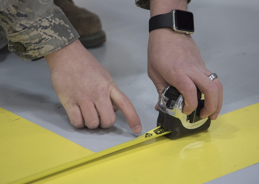 Senior Airman Ivan Abrev, 11th Civil Engineer Squadron structural journeyman, uses a measuring tape at Joint Base Andrews, Md., Feb. 16, 2017. Abrev measured several distances within a hangar to determine where to place an F-16 Fighting Falcon display and U.S. flags in preparation for the Chief Master Sergeant of the Air Force Transition Ceremony. (U.S. Air Force photo by Senior Airmen Jordyn Fetter)