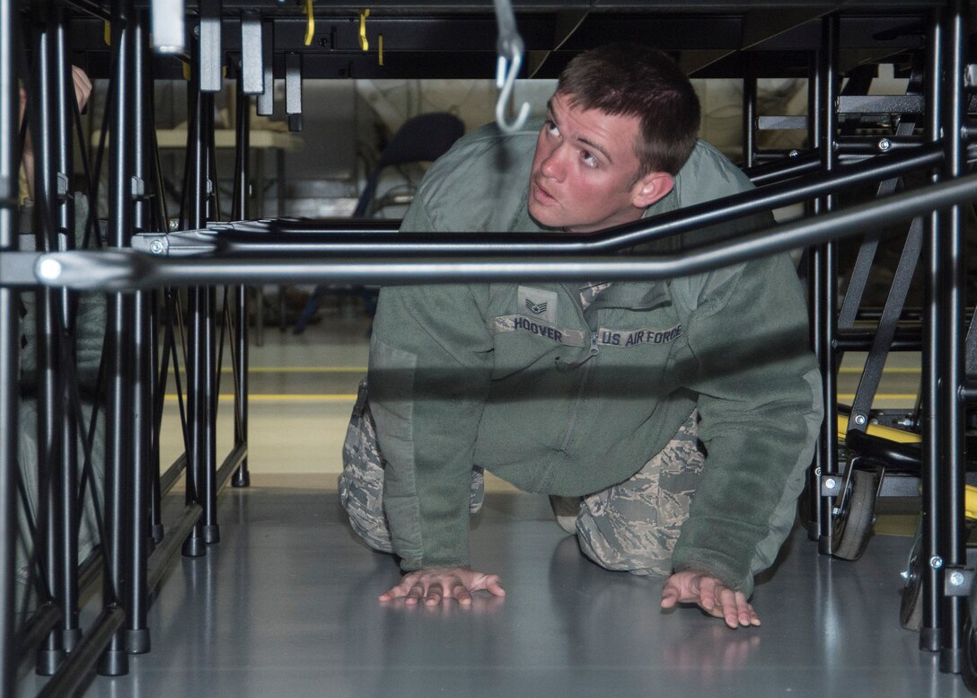 Staff Sgt. Jarret Hoover, 11th Civil Engineer Squadron power production craftsman, crawls under a stage to lock it into place at Joint Base Andrews, Md., Feb. 16, 2017. Airmen from different sections of the 11th CES set up equipment like chairs, bleachers and a stage in preparation for the Chief Master Sergeant of the Air Force Transition Ceremony. (U.S. Air Force photo by Senior Airmen Jordyn Fetter)
