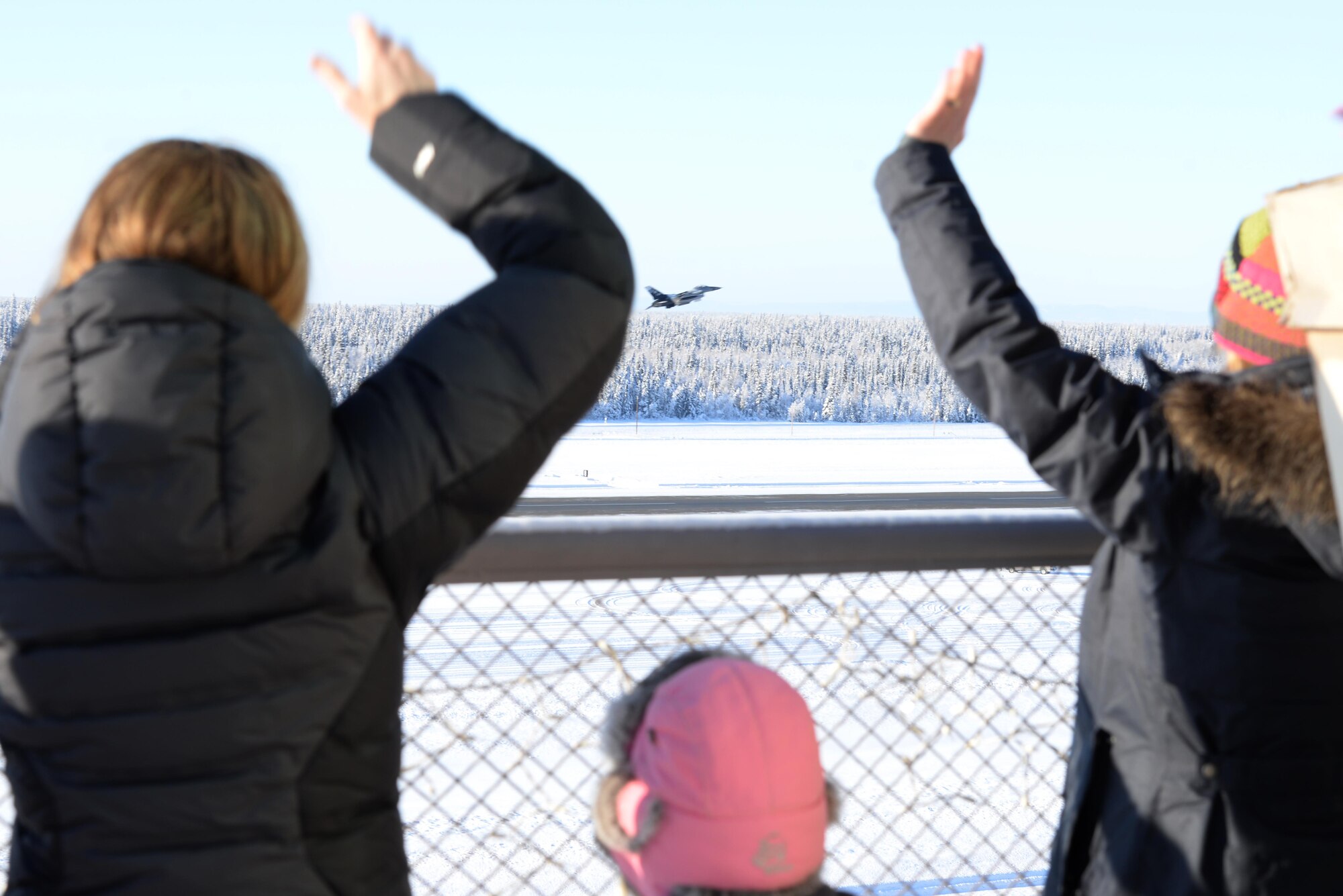 Family members wave goodbye to pilots as they take off Feb. 12, 2017, at Eielson Air Force Base, Alaska. The pilots from he 18th Aggressor Squadron departed to support COPE NORTH 2017, an exercise which provides the opportunity for tri-lateral field training exercises which imnproves combat readiness, develops synergistic humanitarian assistance and/or disaster relief operations, and increases interoperability between the U.S., Royal Australian Air Force and Japanese Air Self-Defense Force. (U.S. Air Force Photo by Airman Eric M. Fisher)