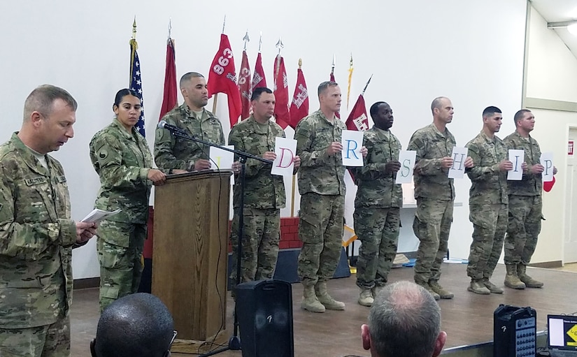 Soldiers stand on stage and hold a piece of paper with an alphabetical letter representing each of the seven Army Values while another Soldier recites the meaning of each value during the 863rd Engineer Battalion’s Non-Commissioned Officer (NCO) Induction Ceremony, signifying the transition from enlisted to the rank of Sergeant at Camp Buerhing, Kuwait, Dec. 8, 2016. (Photo by U.S. Army National Guard Capt. Maria Mengrone/Released)