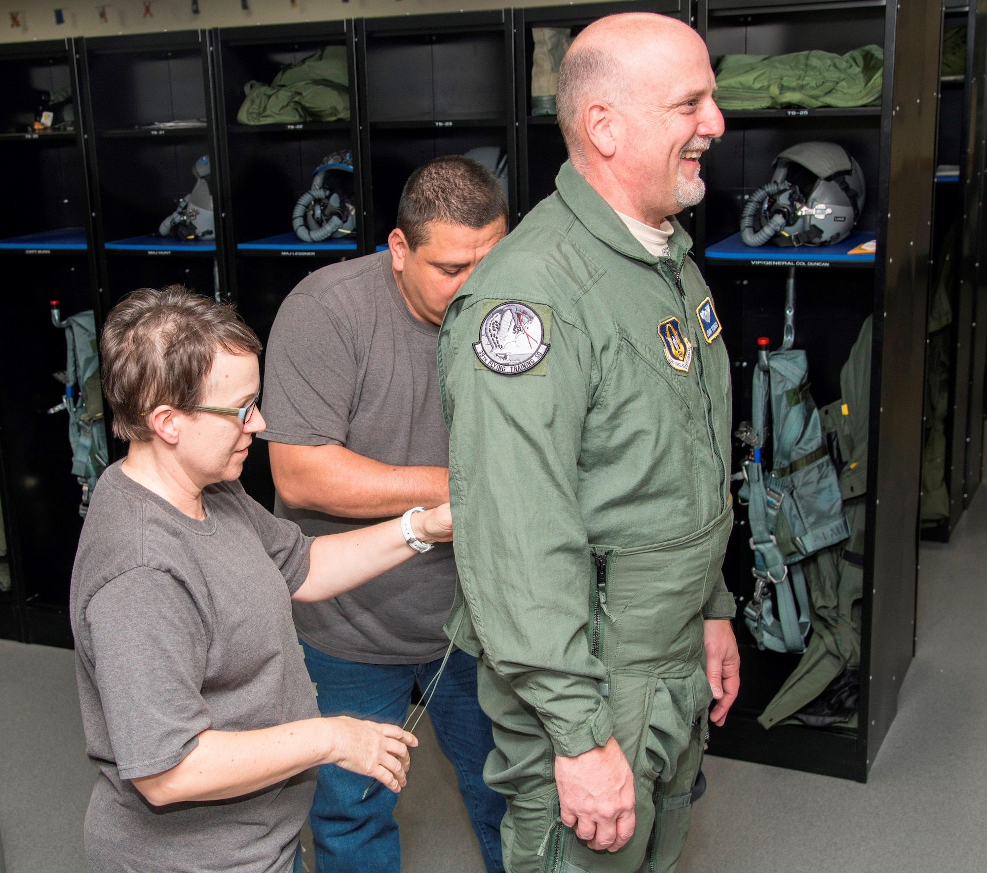 – April Fisher (L) and Eddie Scribner (C) flight equipment life support technicians with the 559 Flying Squadron at Joint Base San Antonio-Randolph, Texas, put the finishing touches on a G-suit for John Fedrico, deputy assistant Secretary of the Air Force for  Reserve Affairs and Airman Readiness in preparation for a T-6 orientation flight here Feb. 13. Fedrico’s visit, hosted by the 340 FTG, served a dual purpose. Fedrico presented a letter of thanks to one of the unit’s own, retired Air Force Lt. Col. Todd Ernst. Ernst was honored for his efforts to help ensure families of Reserve and Guard service members receive the same survivor benefits as active duty service members. Fedrico also received a mission brief and got to experience the unit’s operations first hand. (Air Force photo by Sean Worrell, Joint Base San Antonio-Randolph Public Affairs)