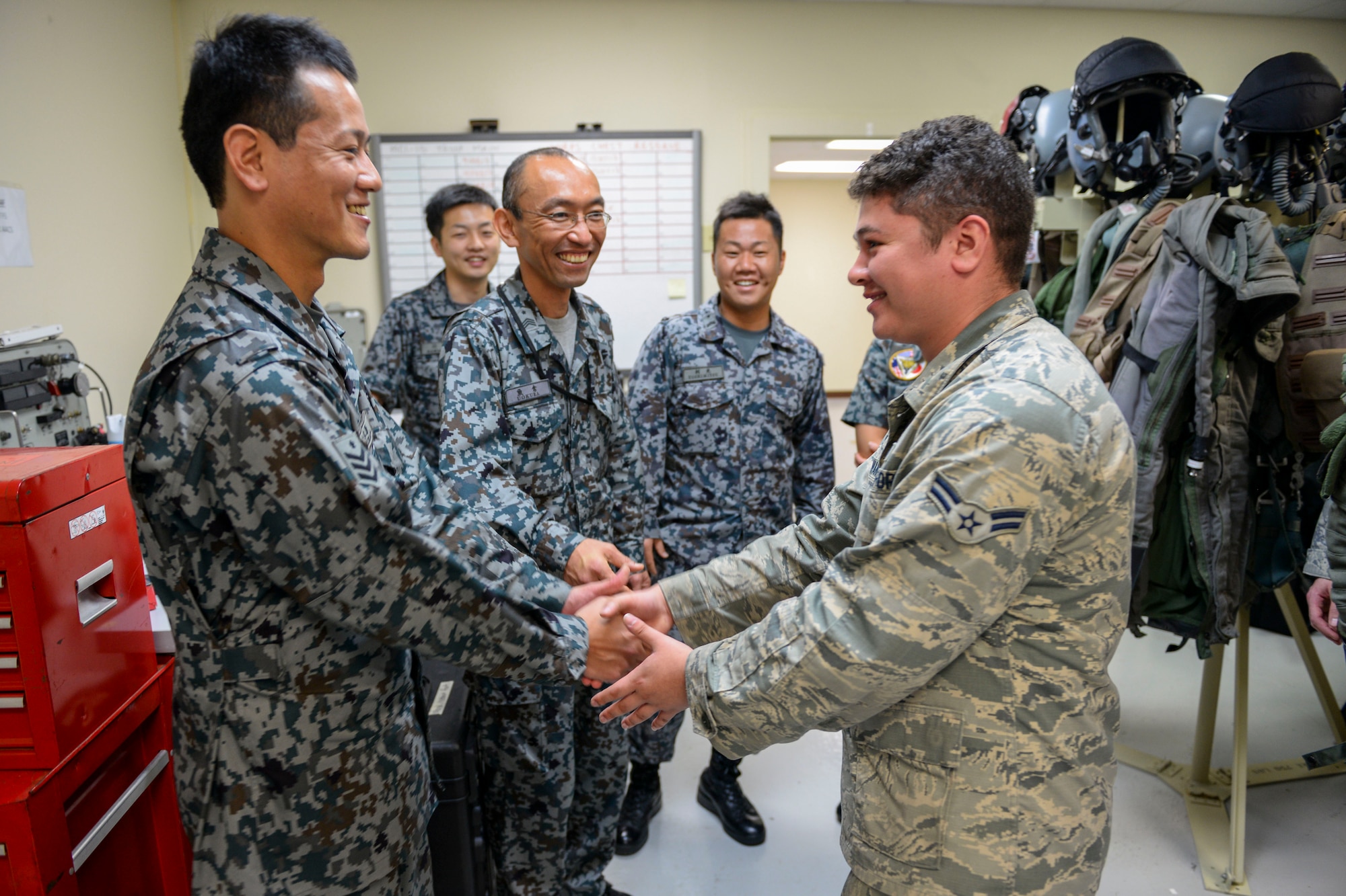 Japan Air Self-Defense Force Airman 1st Class Nobuhiro Kamikiharo, maintenance crew specialist from Tsuiki Air Base, Japan, and U.S. Air Force Airman 1st Class Jesse Inman, 18th Operations Support Squadron aircrew flight equipment apprentice, shake hands Feb. 17, 2017, at Andersen Air Force Base, Guam. Aircrew flight equipment Airmen from both nations are working under the same roof, where they can learn customs from each other’s culture and compare techniques of one another’s craft. (U.S. Air Force photo by Senior Airman John Linzmeier/released)