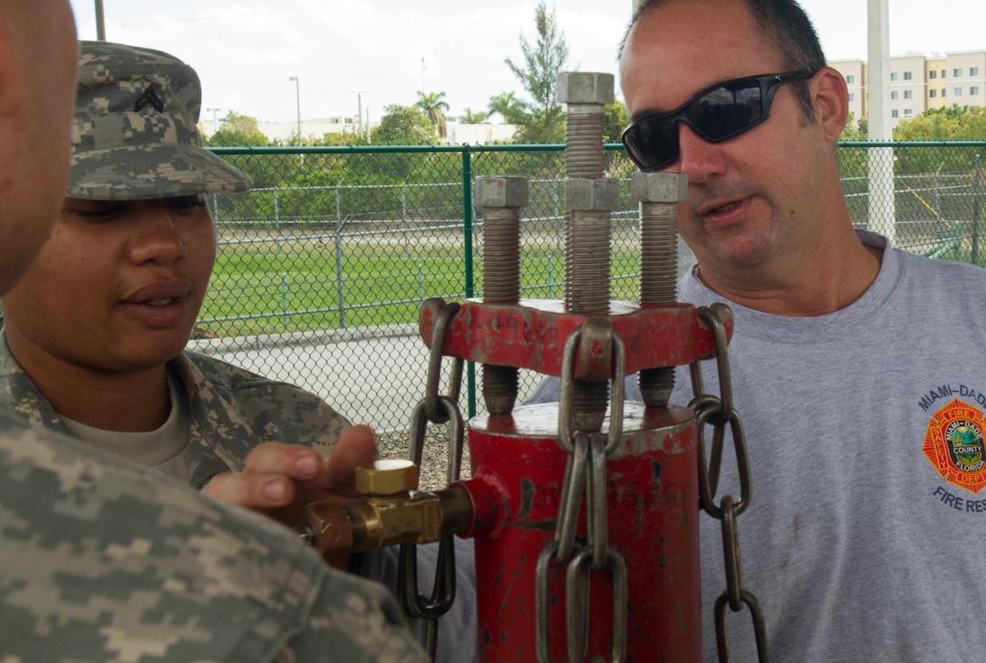 Firefighter David Guerra, a flight medic with the Miami-Dade Fire Rescue Department (MDFR), assists Army Reserve Cpl. Shalandis Johnson on how to cap a gas cylinder during training at the MDFR training facility on Feb. 17, 2017 in Doral, Fla. Johnson, who lives in Orlando, Fla., is a Chemical, Biological, Radiological, and Nuclear (CBRN) Specialist assigned to the 329th CBRN Company (Reconnaissance and Surveillance), which is based in Orlando. The 329th CBRN Company, the Army Reserve’s 469th Ground Ambulance Company, from Wichita, Kan., and the Florida National Guard’s Civil Support Team, spent the day training with MDFR firefighters and learned about tools Soldiers could use if called up to support hazardous material operations in Port of Miami and Dade County. (Army Reserve photo by Master Sgt. Mark Bell / Released)