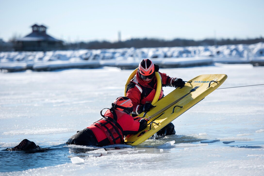 A Coast Guardsman, right, uses a sled to rescue a simulated cold water victim from Lake Champlain during ice water rescue training at Coast Guard Station Burlington, Vt., Feb. 17, 2017. Air National Guard photo by Tech. Sgt. Sarah Mattison
