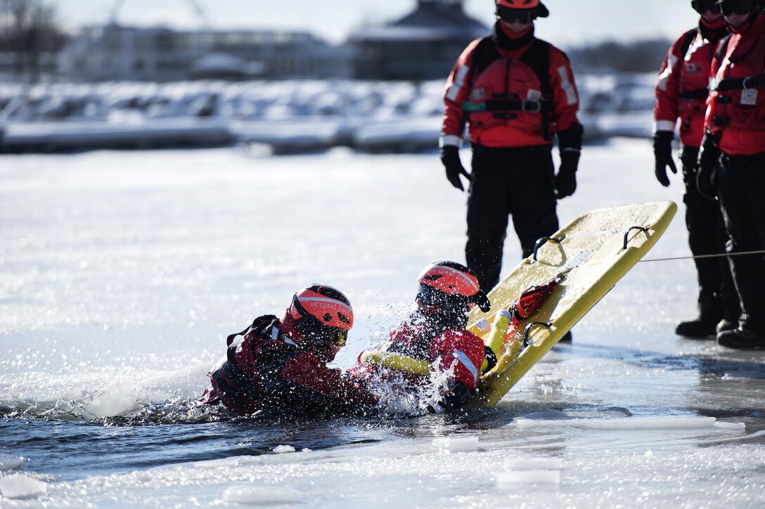 A Coast Guardsman, right, uses a sled to rescue Coast Guard Rear Adm. Steven Poulin, left, commander, First Coast Guard District, role-playing as a simulated cold water victim from Lake Champlain during ice water rescue training at Coast Guard Station Burlington, Vt., Feb. 17, 2017. Air National Guard photo by Tech. Sgt. Sarah Mattison