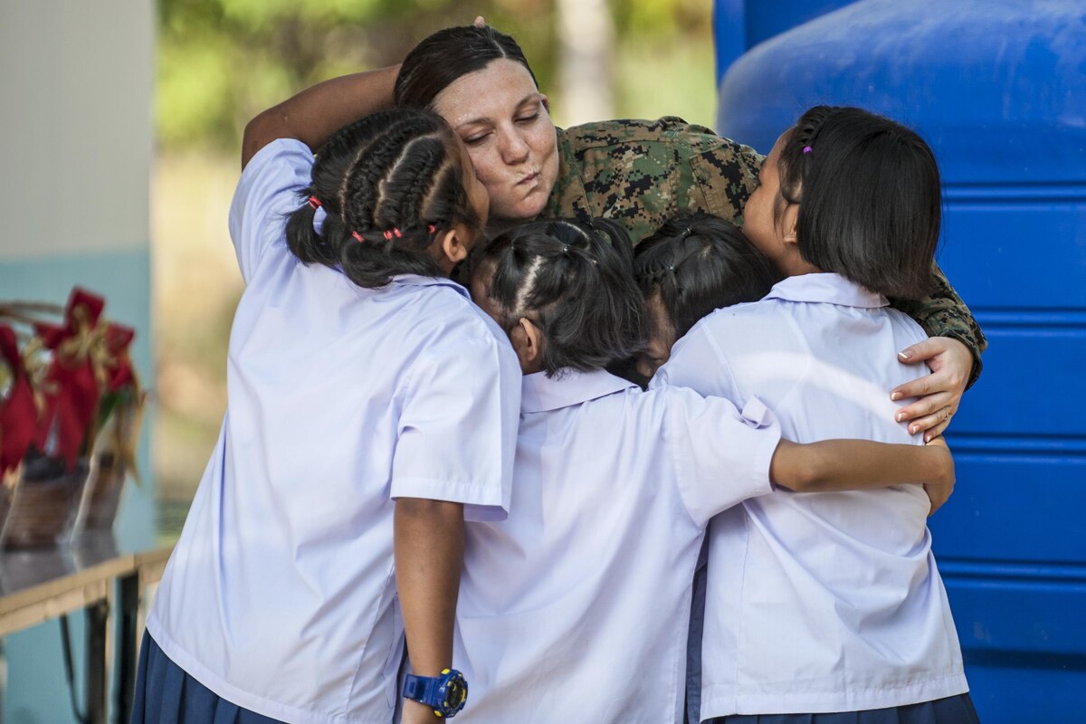 A sailor bids farewell to Thai students with a group hug.