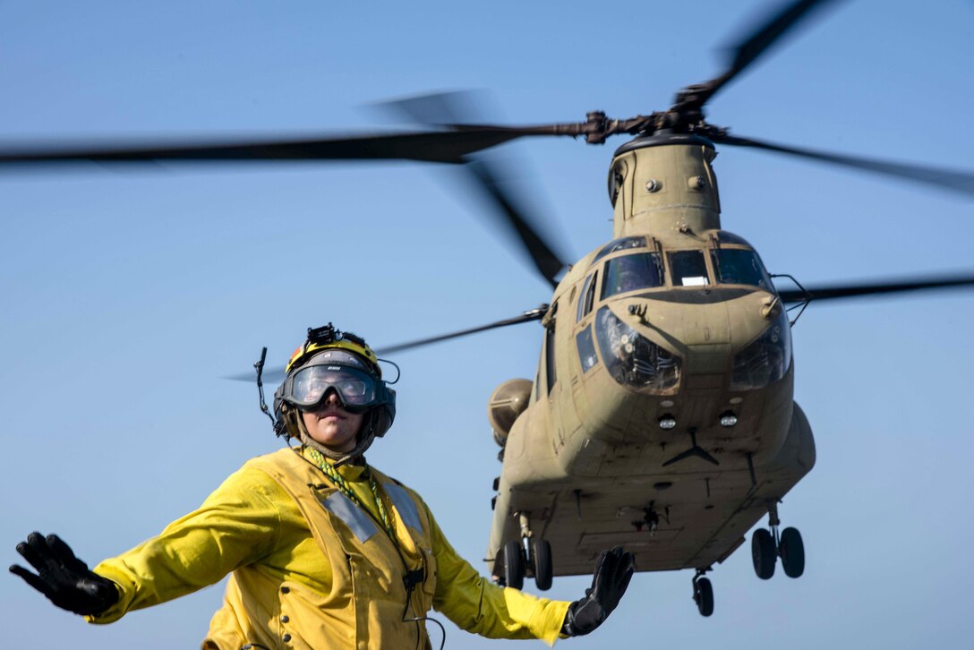 Navy Petty Officer 3rd Class Julia Valles signals to personnel to stand clear as an Army CH-47F Chinook helicopter takes off from the USS Green Bay during Cobra Gold 2017 in the Gulf of Thailand, Feb. 21, 2017. The exercise aims to strengthen engagement in the region. Valles is an aviation boatswain’s mate (handling). Navy photo by Petty Officer 1st Class Chris Williamson
